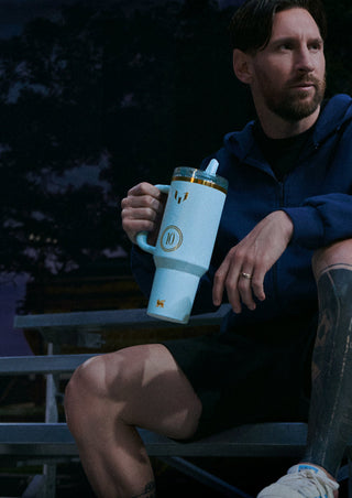 Messi sitting outdoors at night holding a light blue mug with a straw.