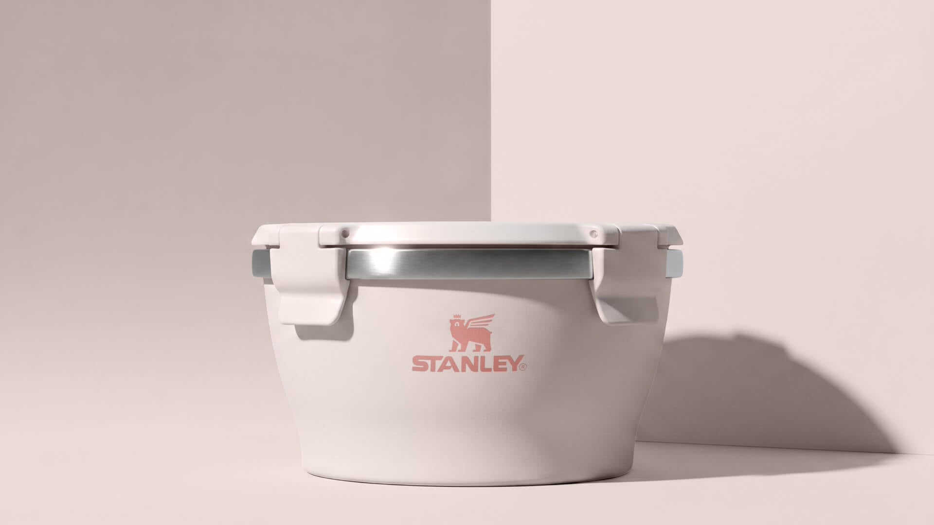 A white Stanley cooler with a silver lid and a red logo on the front, set against a minimalist beige background with a soft shadow.