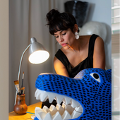 Woman sitting at a desk with a large blue and white dragon head sculpture, surrounded by art supplies.