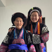 Two people in traditional attire standing against a white wall.