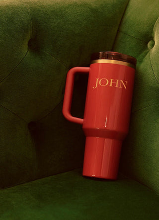 Red thermos with 'JOHN' branding on a green cushioned surface