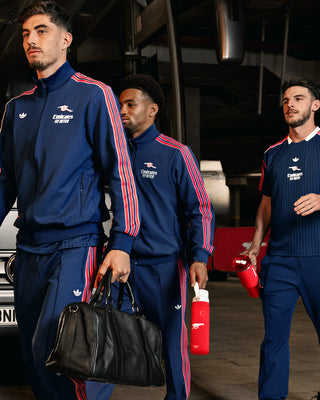 Three men in matching blue tracksuits with red stripes walking in a garage.