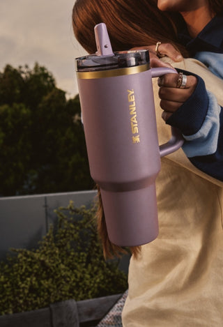 Person holding a pink Stanley tumbler with a blurred outdoor background