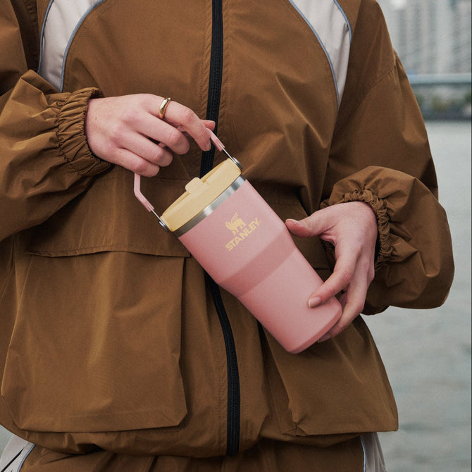 Model holding a pink Stanley 1913 IceFlow Flip Straw Tumbler with a blurred cityscape background
