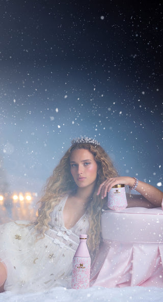 Woman in a white dress with a tiara holding a pink bottle in a snowy setting