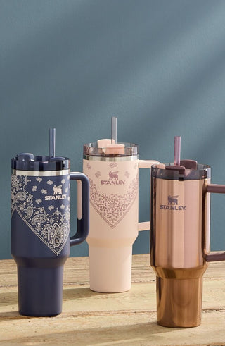 Four insulated travel mugs with handles on a wooden surface against a blue background