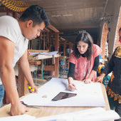 Three people working together on a project with a tablet at a table.