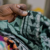 Close-up of a hand holding a piece of green fabric with black patterns, blurred background