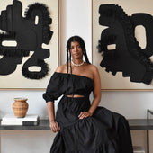 Woman in a black outfit sitting on a bench in a room with abstract art on the wall.