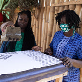 Two women working with a printing press in an outdoor setting.